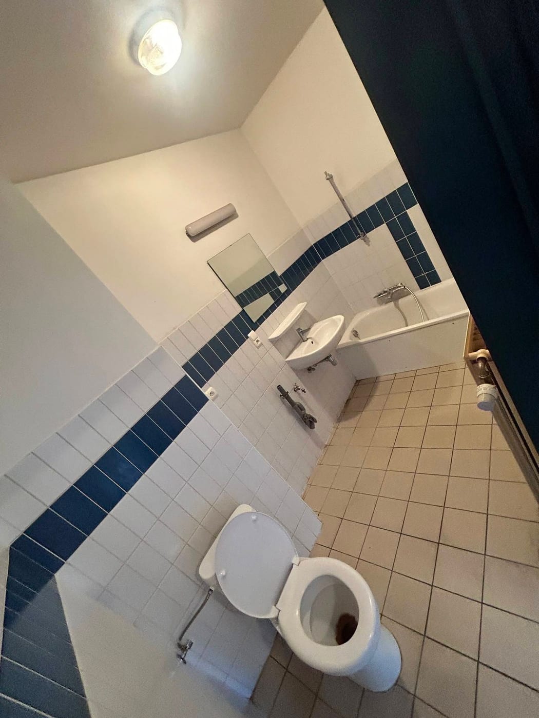 Leeggemaakte badkamer met een donkerblauwe tegelband, een lege badkuip, een lavabo en een vrijstaand toilet