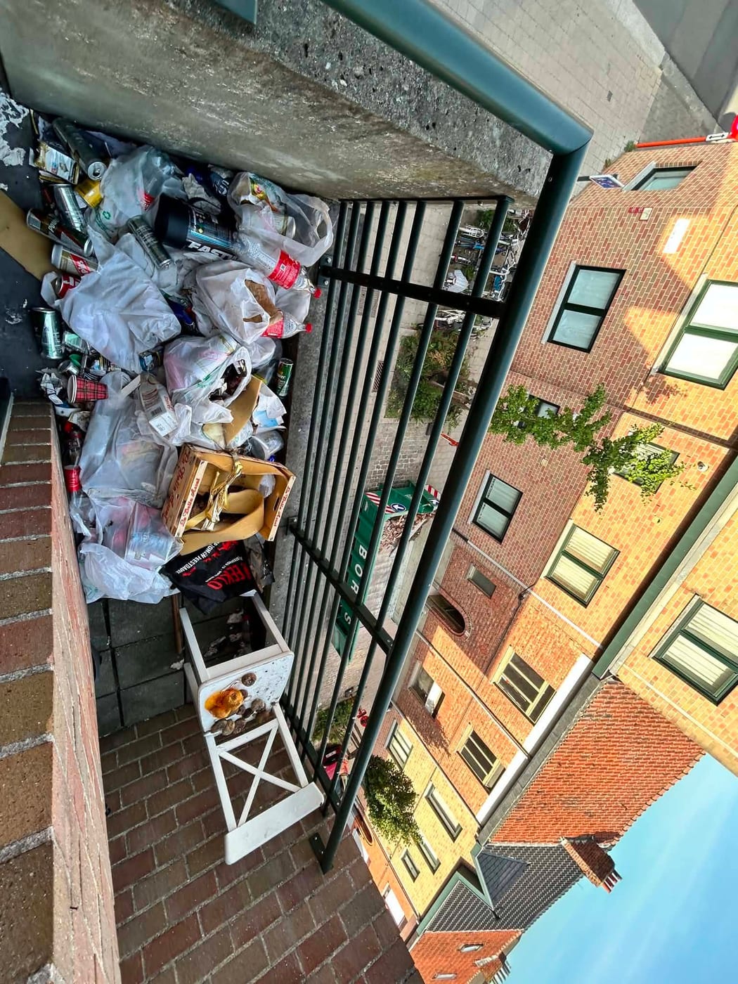 Balkon van bovenaf gezien, tot tegen de balustrade volgestapeld met zakken, dozen en meubelstukken