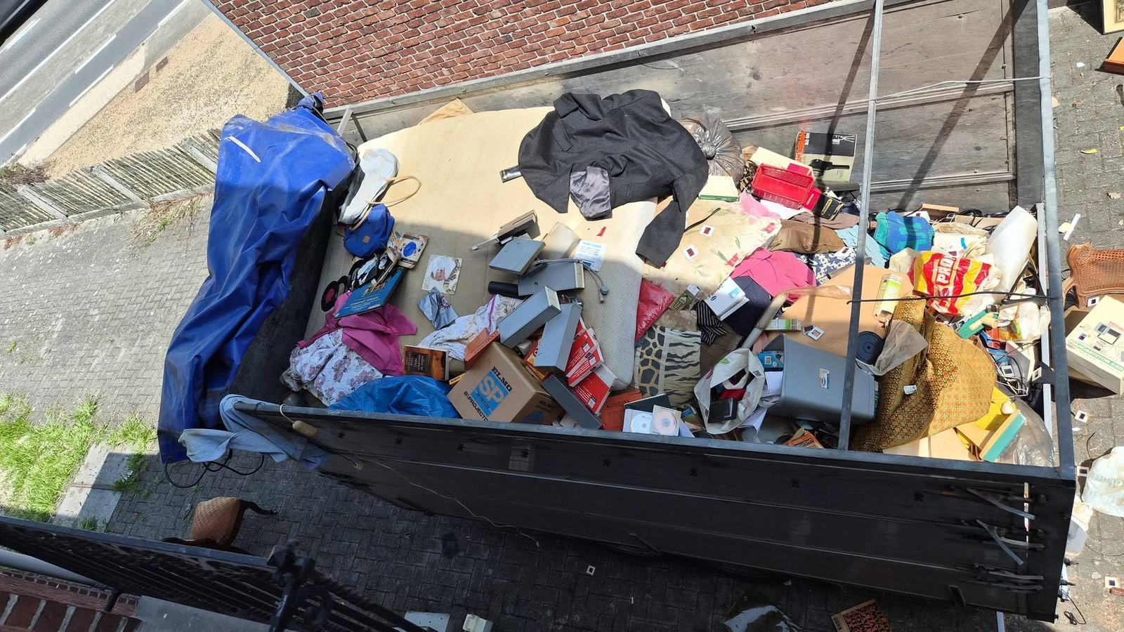 Container aan de gevel, tot bovenaan gevuld met huisraad uit een ontruimde woning