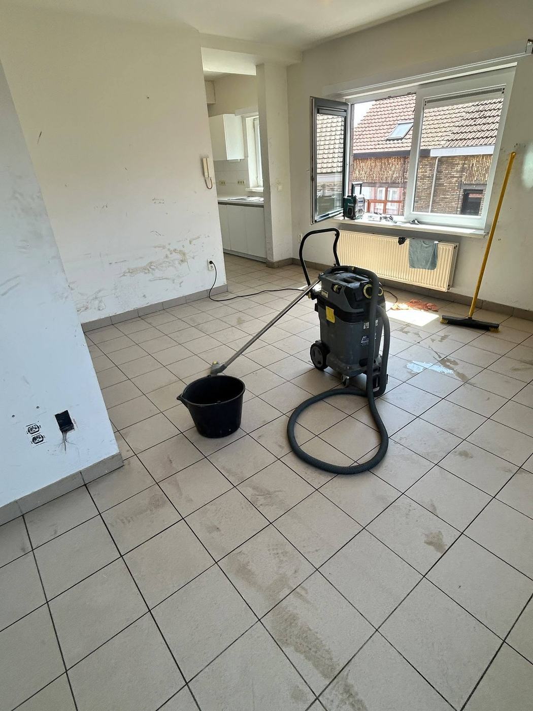 Waterstofzuiger en emmer midden in een leeggemaakt appartement tijdens de dieptereiniging