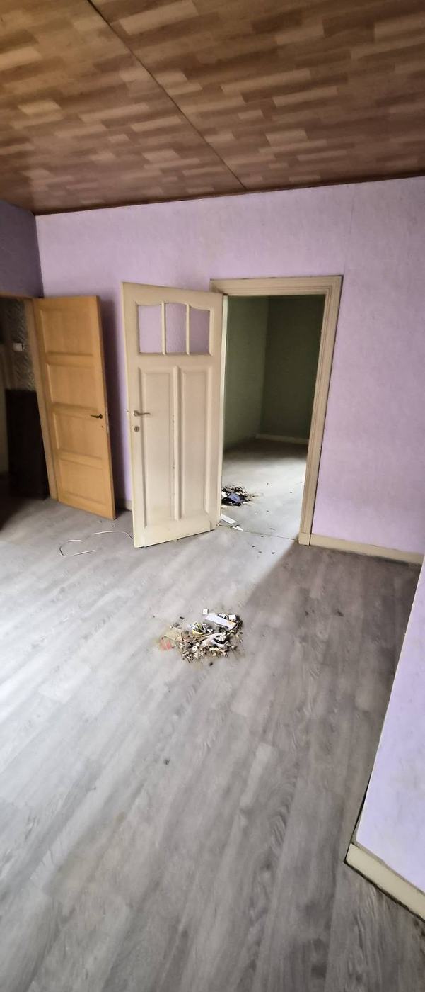 Leeggehaalde kamer met open binnendeur en geveegde laminaatvloer na de ontruiming