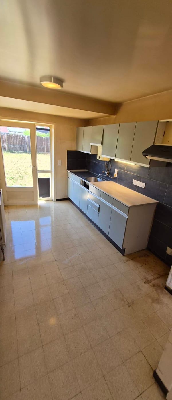 Leeggemaakte keuken met grijze kasten en tuindeuren, met de vloer pas gedweild