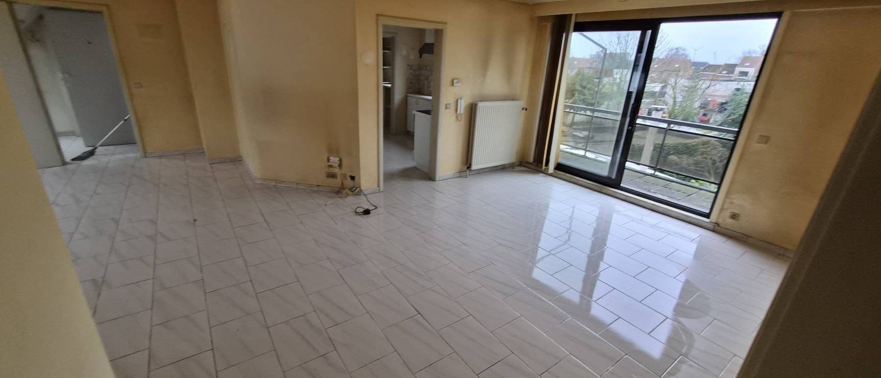 Leeggemaakte living van een appartement met groot raam en gedweilde vloer na de eindschoonmaak