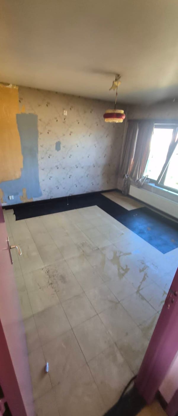 Dezelfde slaapkamer leeg, met dezelfde hanglamp met franjekap, hetzelfde gestripte muurvlak en een lege tegelvloer