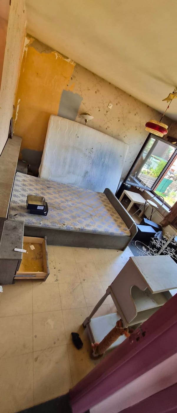 Slaapkamer met een matras op een bedbodem, een opengetrokken lade en achtergelaten meubels op de tegelvloer, onder een hanglamp met franjekap